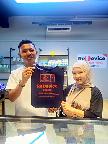 Pasangan tersenyum memegang beg ReDevice di kaunter kedai